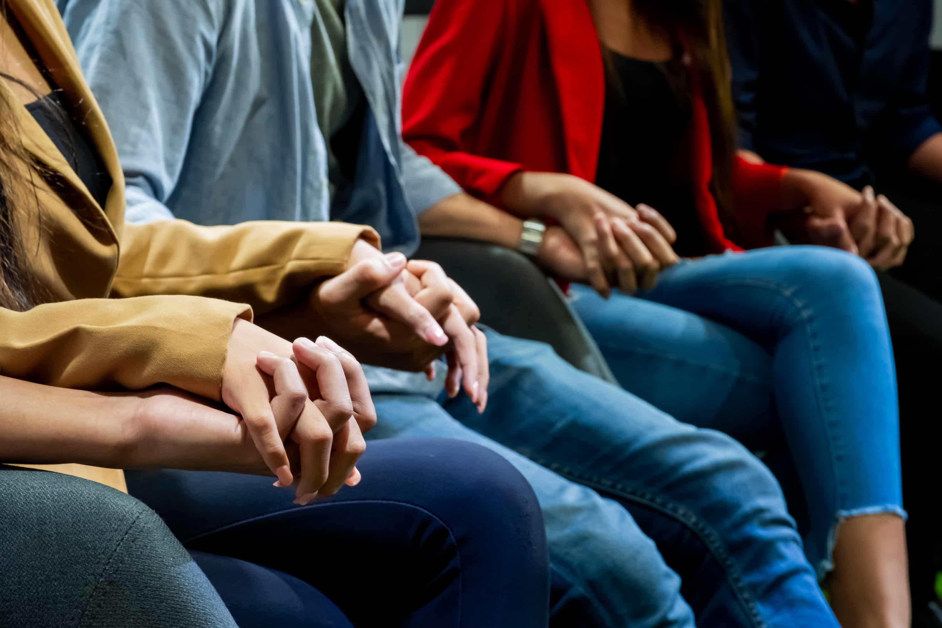 Image of a support meeting where all are sitting and holding
                                            hands