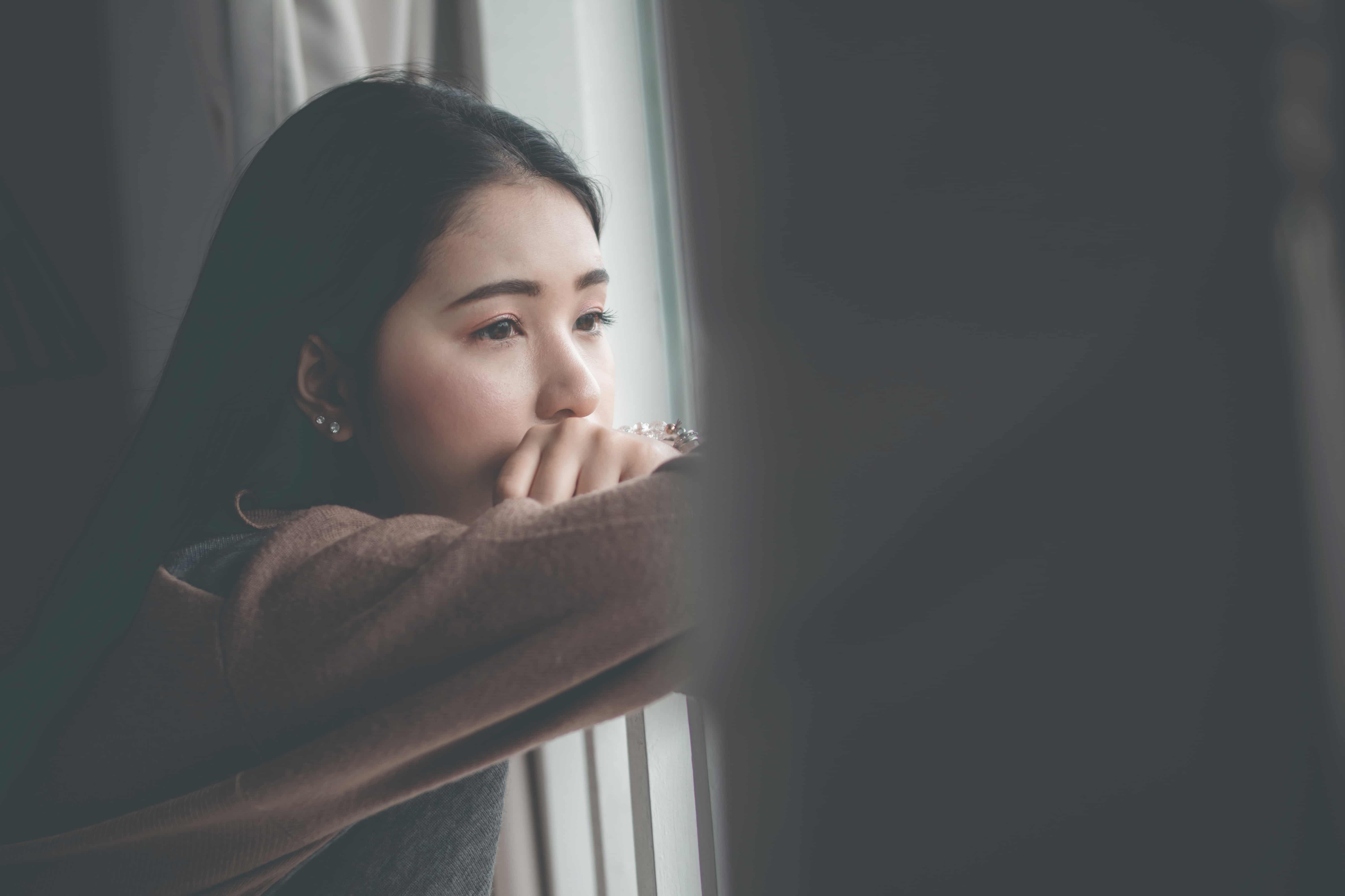 Image of an adult woman looking through a window, stoic