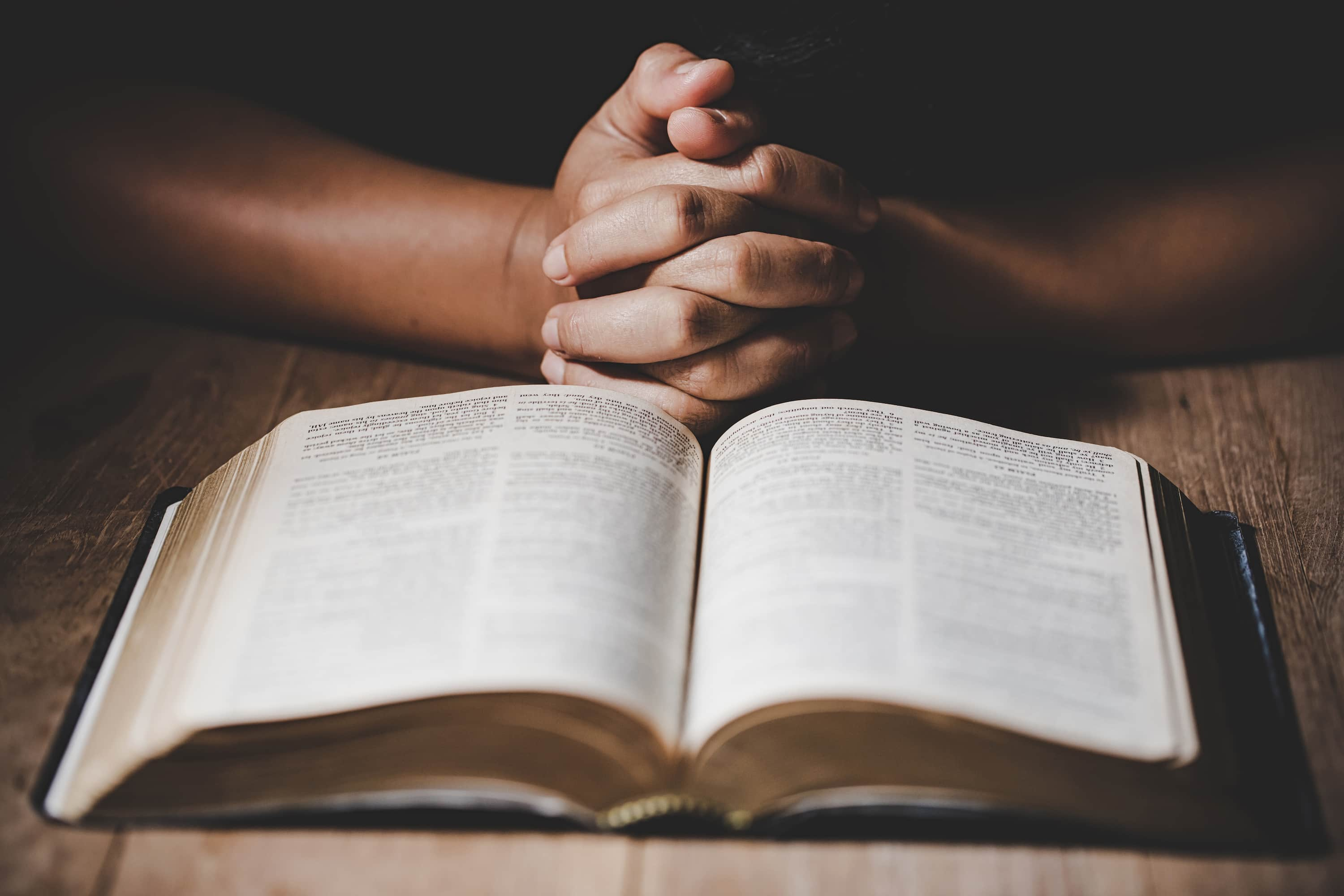 Image of an open Bible with a pair of hands folded above it